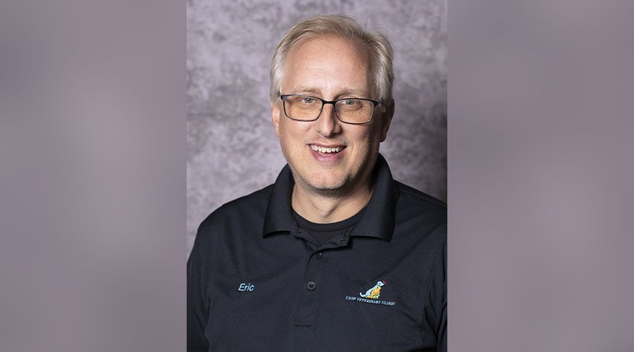 Smiling man with glasses wearing a black polo shirt embroidered with a logo.