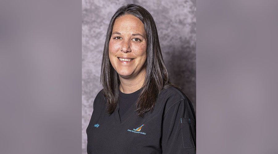 Woman with long hair smiling, wearing a black polo with an embroidered logo.
