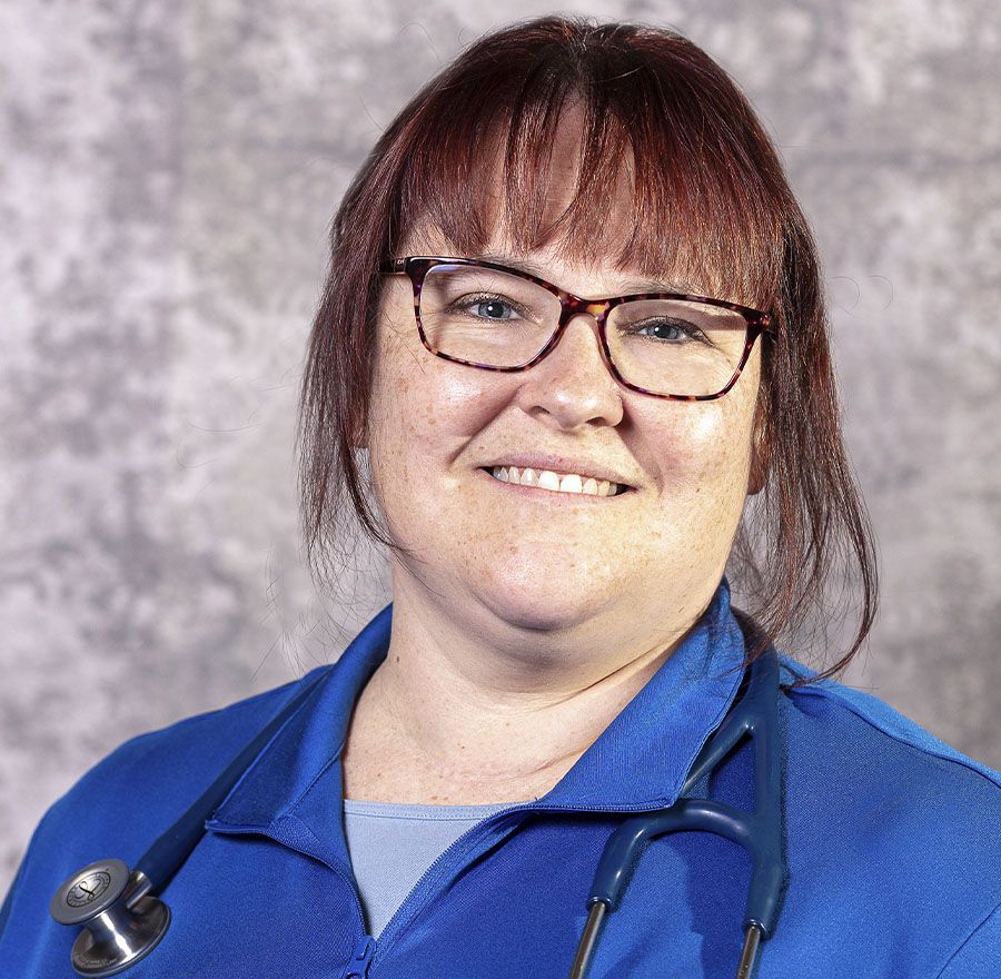 Smiling woman in blue scrubs with glasses and a stethoscope.