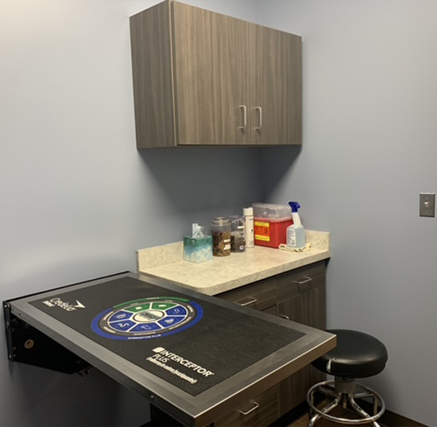 Medical office counter with supplies and a stool under an overhead cabinet.